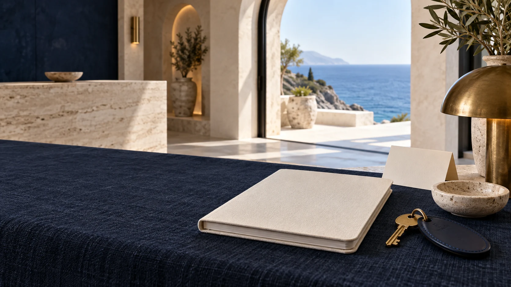 Original hospitality identity: navy linen, an ivory guest folio and a brass room key beside the sea