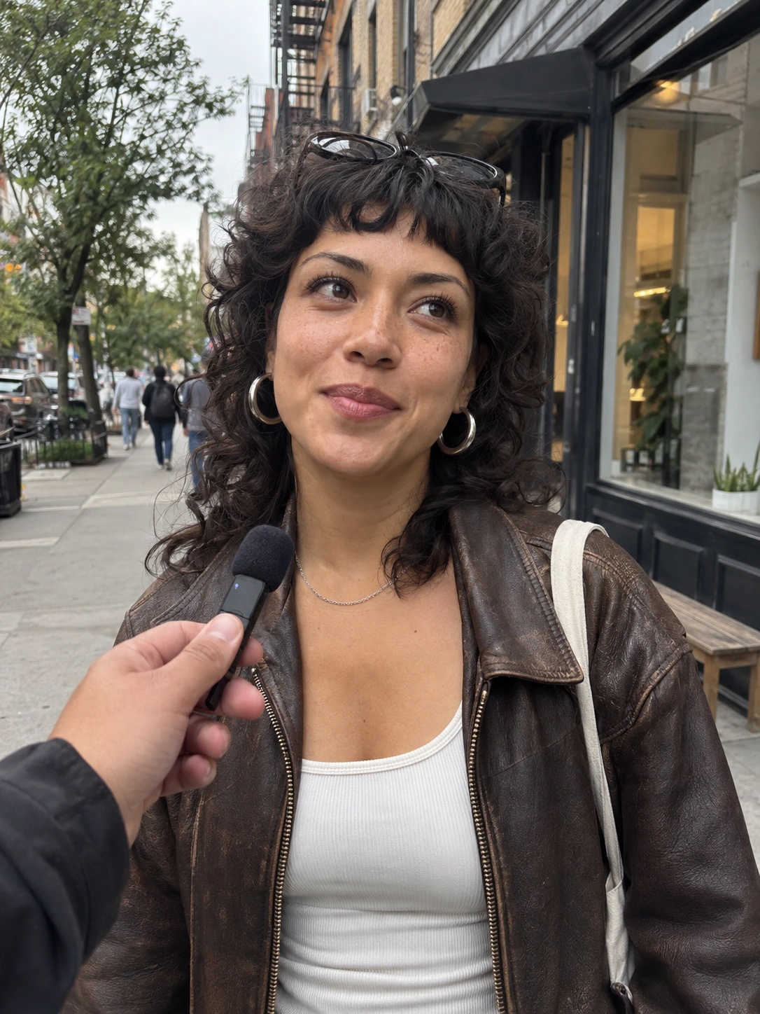 Fashion-forward woman with a curly shag, leather bomber and silver hoops answering a sidewalk interview